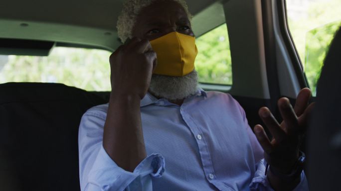 非裔美国老人戴着口罩坐在车里用智能手机聊天