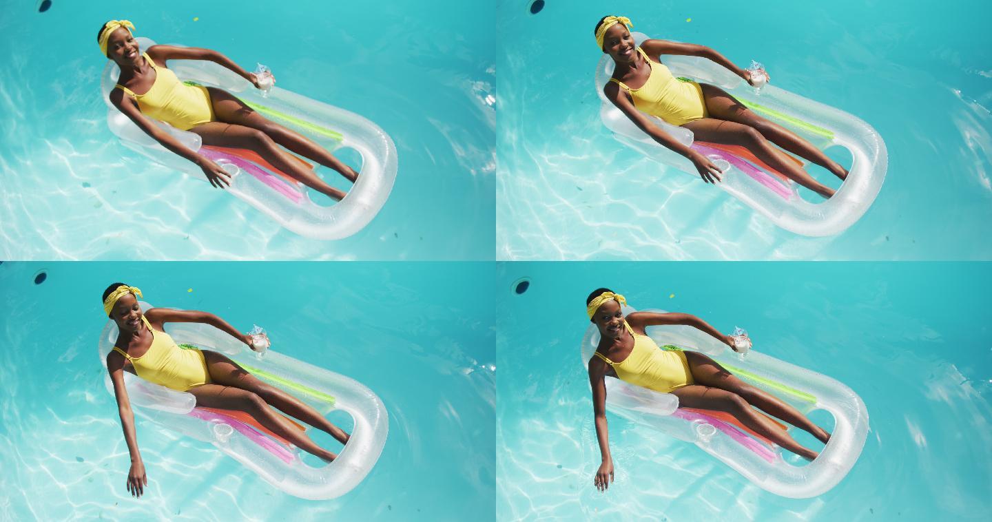迷人的非洲裔美国女人躺在充气抱着饮料和微笑在游泳池