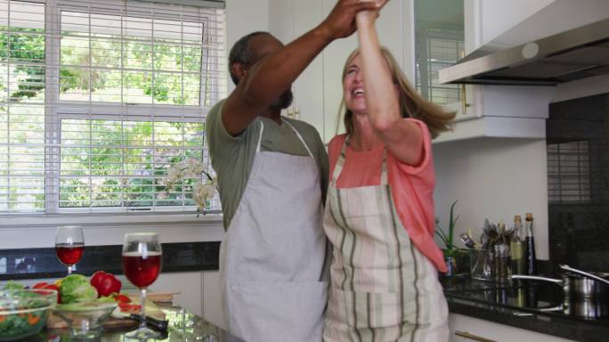 身穿围裙的各种老年夫妇在厨房准备食物时翩翩起舞