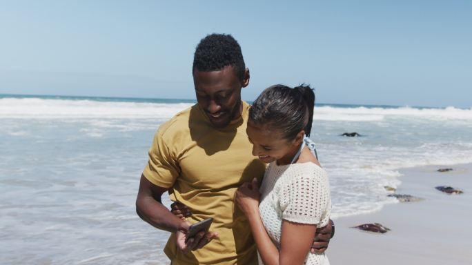 快乐的非裔美国夫妇在海滩用智能手机自拍