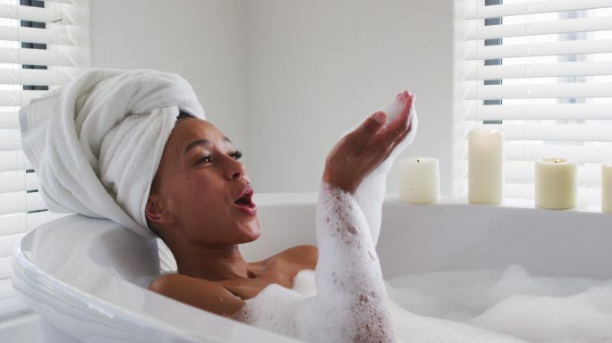 一个非裔美国妇女，在家里浴室的浴缸里吹肥皂泡