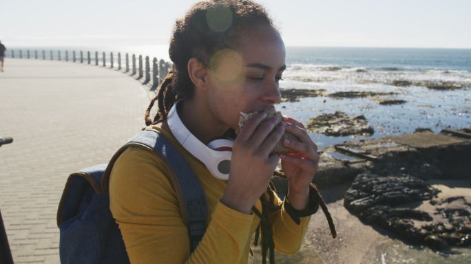 非裔美国妇女坐在海边散步吃三明治