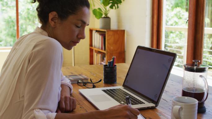 Caucasian woman using laptop and writing, working 