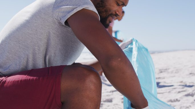 一对非洲裔美国夫妇拿着垃圾袋，在海滩上捡垃圾