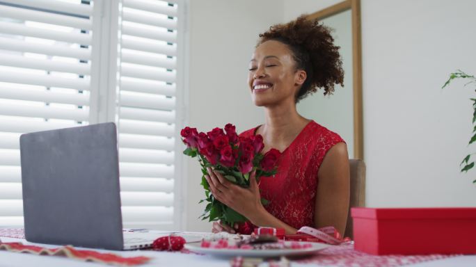 快乐的混合种族妇女在情人节约会视频电话，拿着粉红色的玫瑰