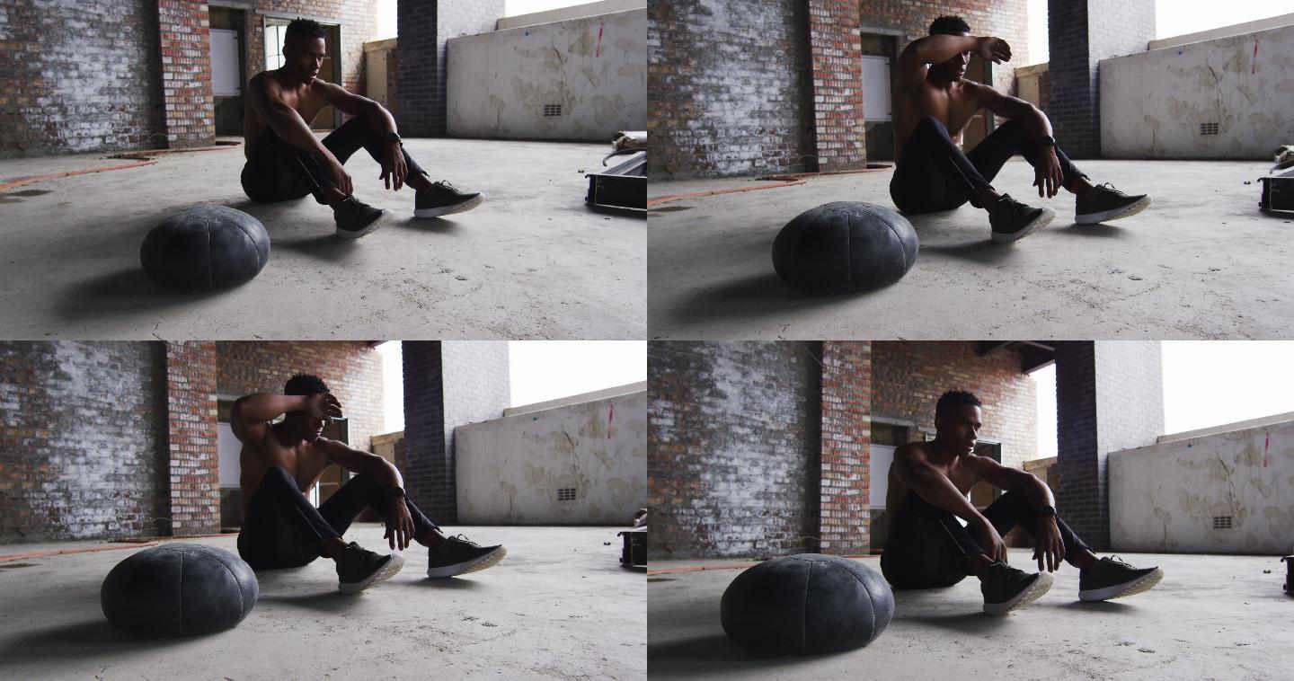 非裔美国人坐在休息后运动与实心球在一个空的城市建筑
