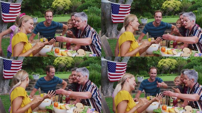 微笑的白人家庭庆祝餐在花园里一起看智能手机