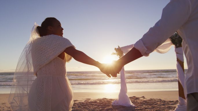 相爱的非裔美国人结婚，在日落时分的海滩上牵着手