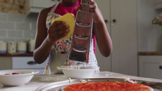 非裔美国女孩在厨房做披萨把奶酪磨碎