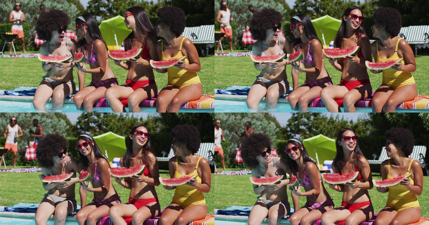 一群不同的女孩拿着西瓜坐在游泳池边聊天