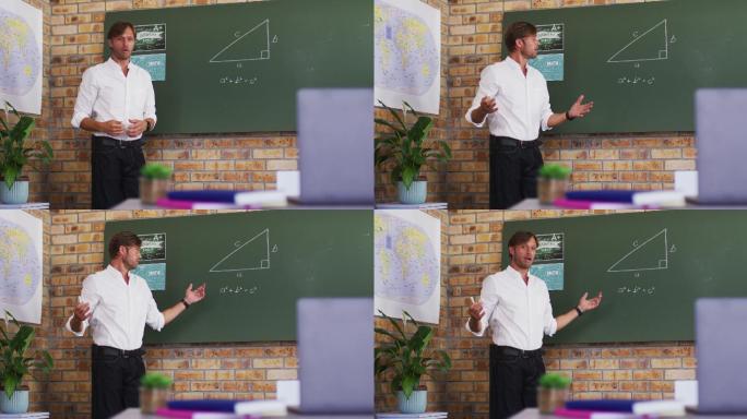 白人男教师在学校的教室里一边教数学一边看着笔记本电脑