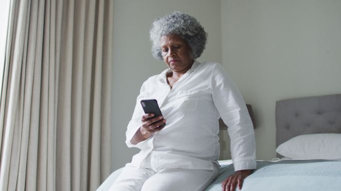 非裔美国老年妇女坐在家里的床上使用智能手机