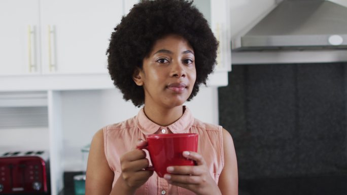 非裔美国妇女在厨房里拿着咖啡杯微笑的肖像