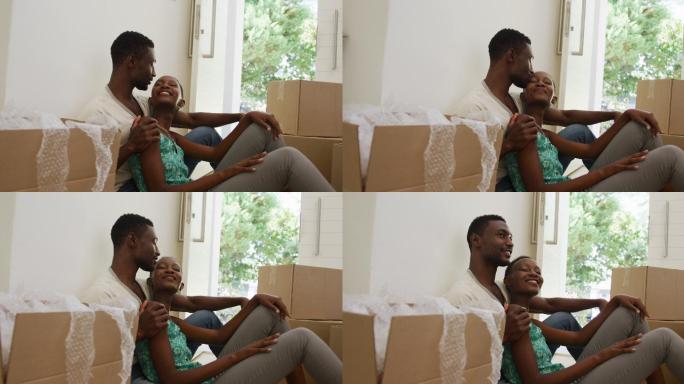 快乐的非裔美国人情侣在地板上交谈和亲吻，坐在包装箱上