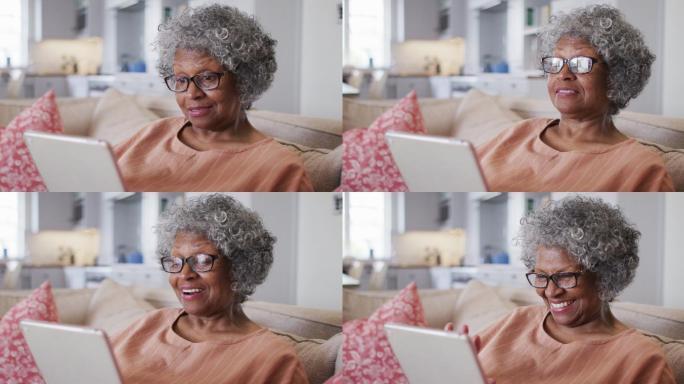 高级非洲裔美国妇女有一个数字平板电脑上的视频聊天，而坐在沙发上的ho