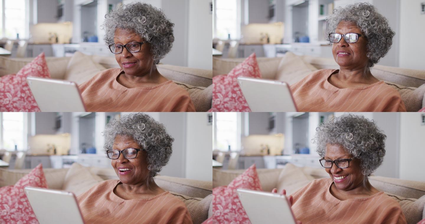 高级非洲裔美国妇女有一个数字平板电脑上的视频聊天，而坐在沙发上的ho
