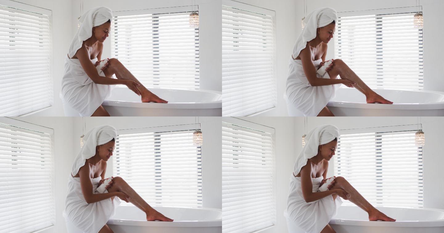 一位非洲裔美国妇女在家里的浴室里往腿上涂保湿霜