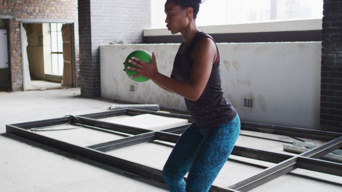 非裔美国妇女在一个空的城市建筑中练习实心球