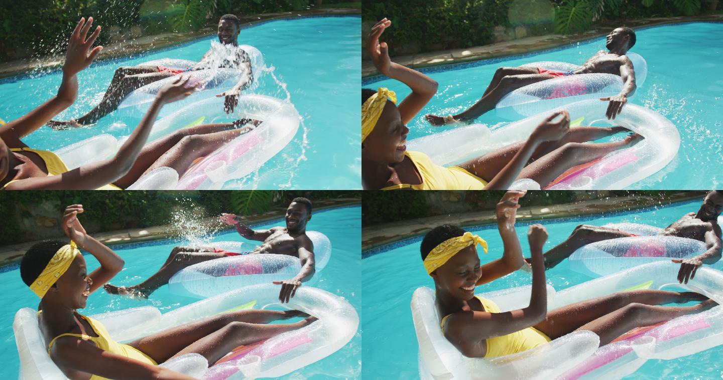 快乐的非裔美国夫妇躺在游泳池里的充气玩具上，微笑着互相溅起水花