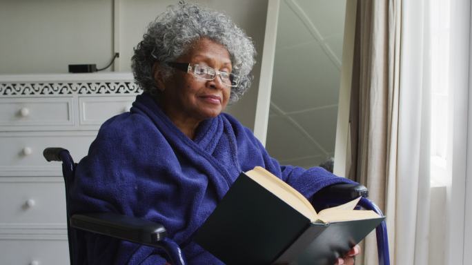 高级非洲裔美国妇女坐在轮椅上在家里看书