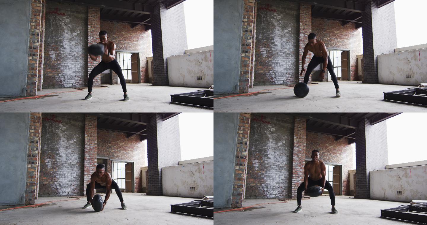 赤膊的非裔美国人在一个空的城市建筑里用实心球锻炼