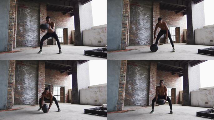 赤膊的非裔美国人在一个空的城市建筑里用实心球锻炼