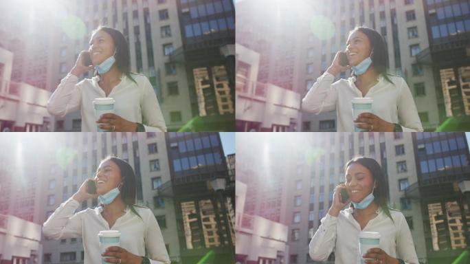 非裔美国妇女戴着面具拿着咖啡用智能手机聊天