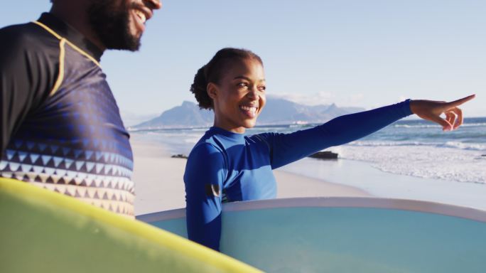 一对非洲裔美国人在沙滩上一边聊天一边拿着冲浪板