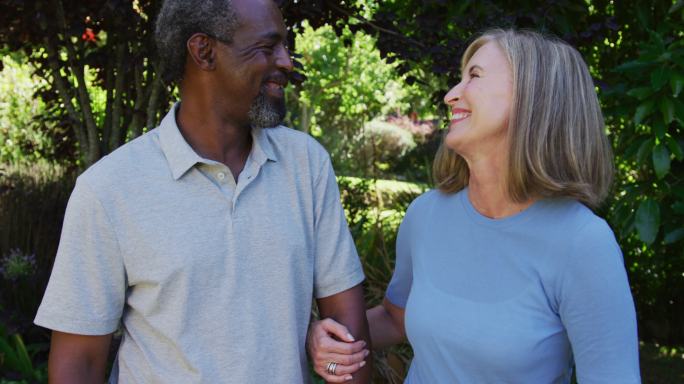 Diverse senior couple walking in their garden arm 