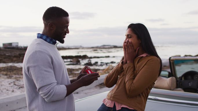 一名非洲裔美国男子在公路上敞篷车旁用戒指向女友求婚