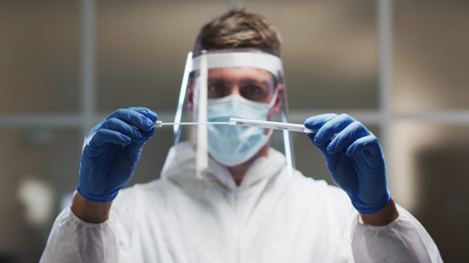 白人男性医务工作者穿着防护服和面罩在实验室检查dna拭子