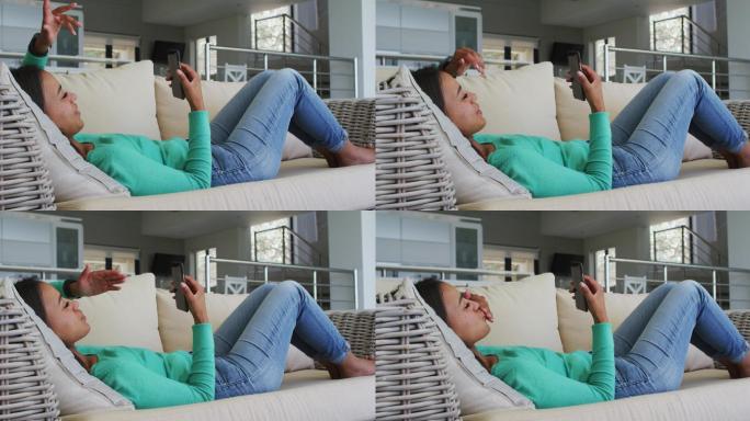 混血女子躺在沙发上用智能手机视频聊天飞吻