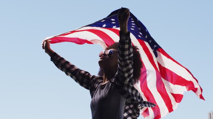 一位戴着太阳镜的非裔美国妇女在空中举着美国国旗