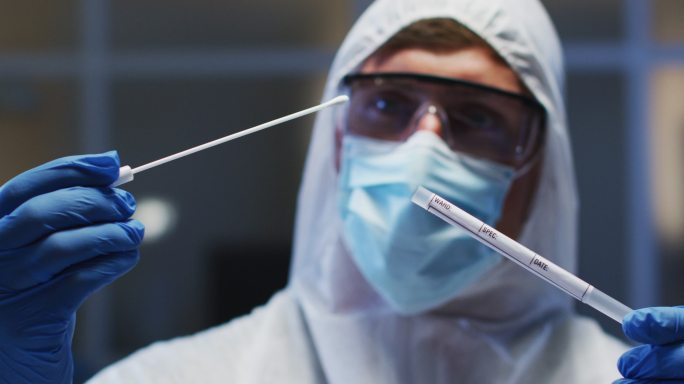 白人男性医务工作者，穿着防护服，戴着口罩和手套，在实验室检查dna拭子