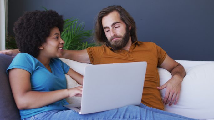 混血夫妇坐在沙发上使用笔记本电脑在客厅