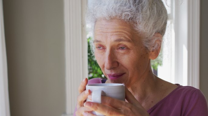 白人老年妇女一边喝咖啡一边看着窗外的特写镜头