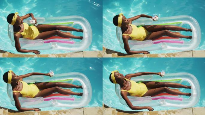 迷人的非洲裔美国女人躺在充气抱着饮料和日光浴在游泳池