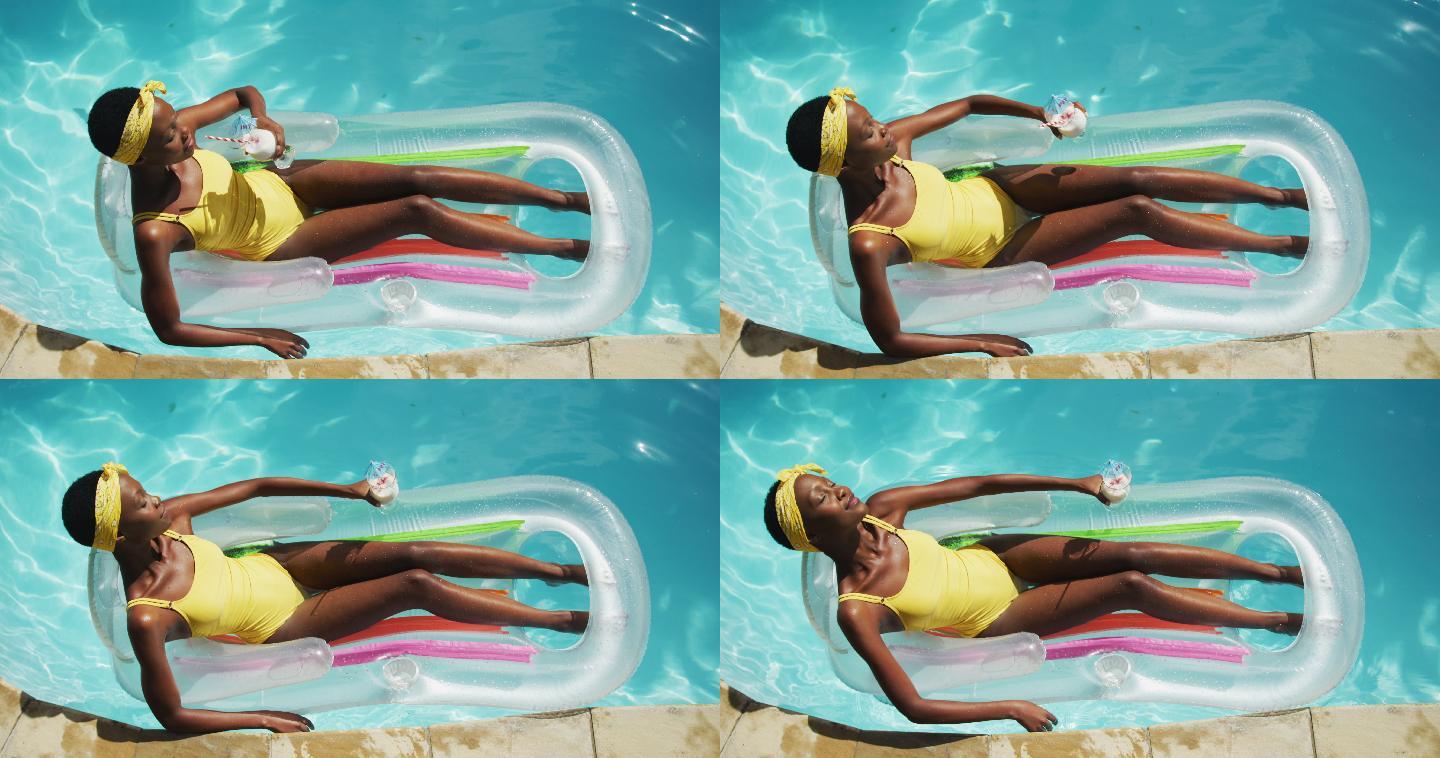 迷人的非洲裔美国女人躺在充气抱着饮料和日光浴在游泳池