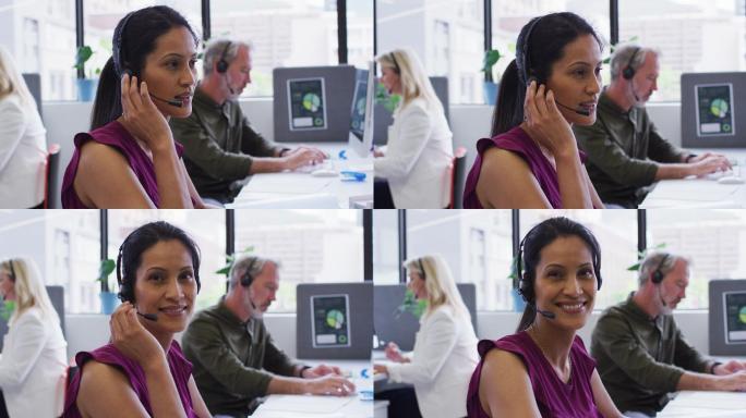 肖像的混血女商人坐在使用电脑在办公室讲电话耳机