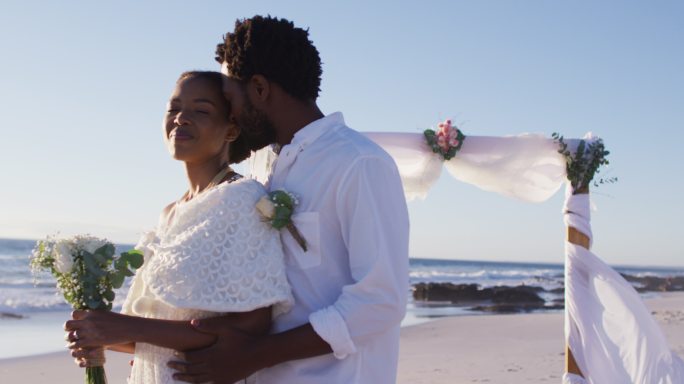 一对非裔美国情侣在海滩上结婚，拥抱，微笑