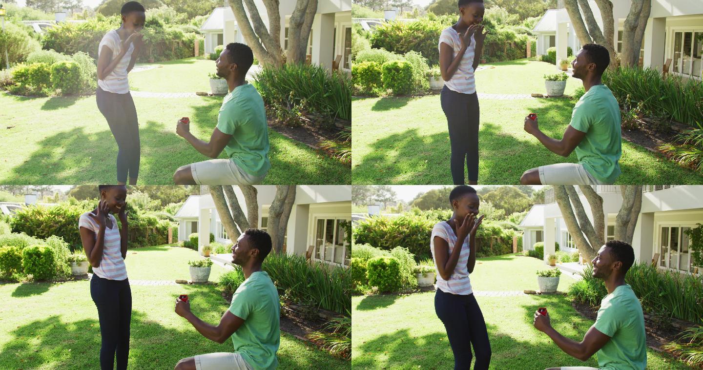 幸福的非裔美国夫妇在阳光灿烂的花园男人跪着拿着戒指向女人求婚