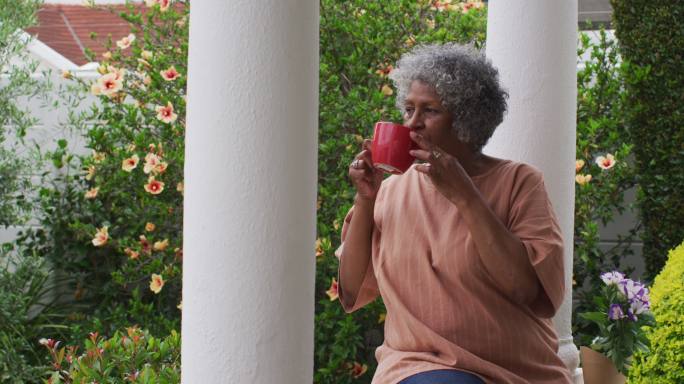 高级非洲裔美国妇女坐在房子的门廊上喝咖啡