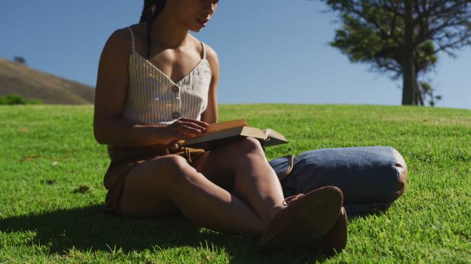 一位非裔美国妇女坐在公园的草地上看书