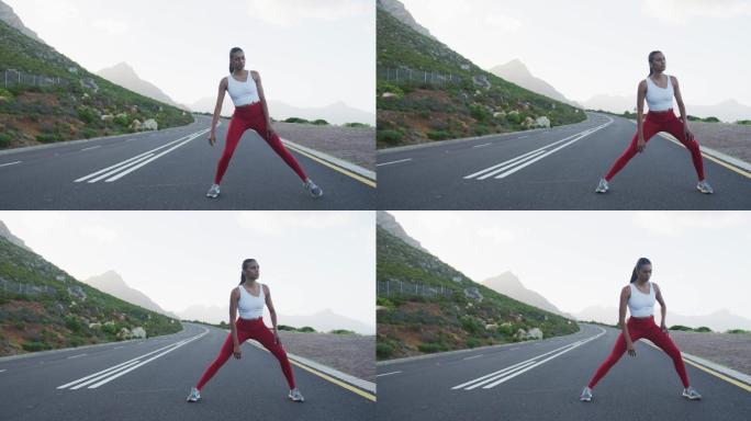 适合混合种族妇女锻炼伸展在一个乡村公路附近的山