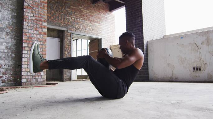 一个非裔美国人在一个空的城市建筑里用实心球锻炼