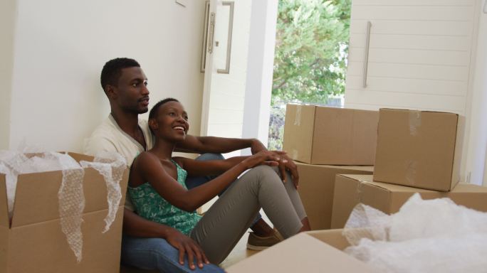 快乐的非裔美国人夫妇拥抱交谈坐在地板上与包装盒