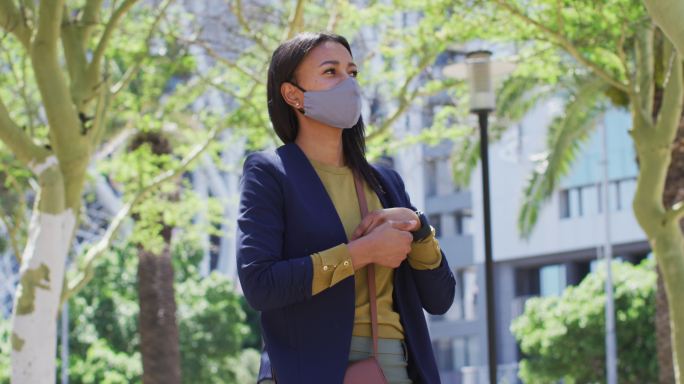 非洲裔美国妇女戴着口罩在街上给双手消毒