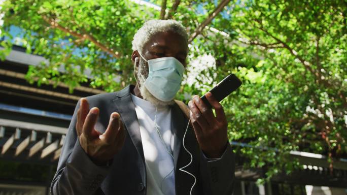 非裔美国高级男子戴着口罩在公司园区用智能手机聊天