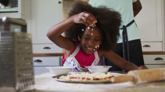非裔美国人的女儿在厨房做披萨，她的父亲在后台做饭