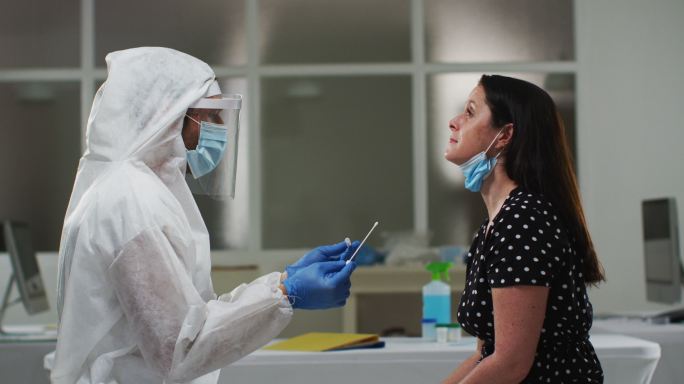 穿着防护服的医务人员对女性患者进行拭子测试